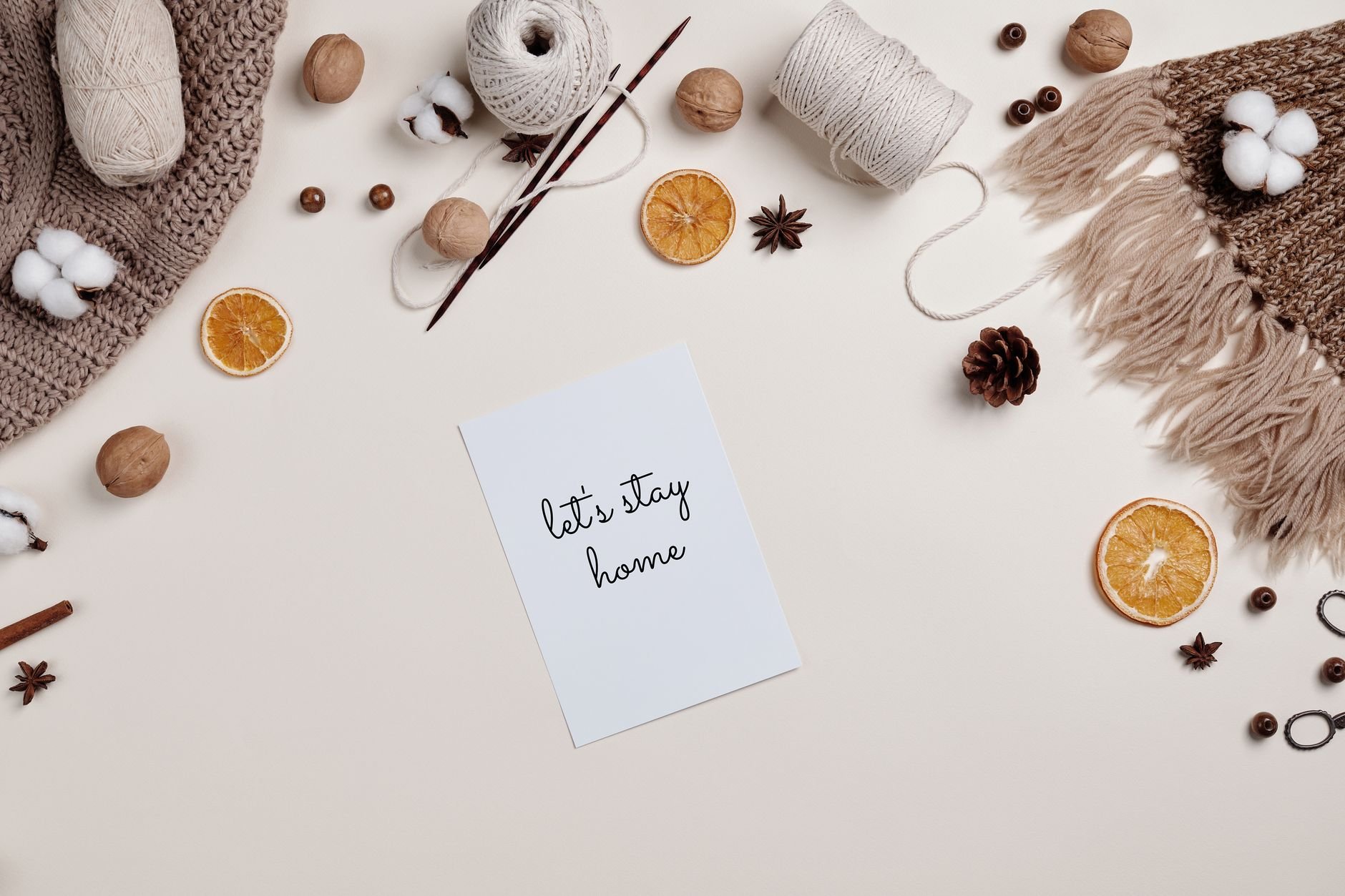 Flatlay of knitting materials, orange slices, and cozy decor with a 'Let's Stay Home' note.